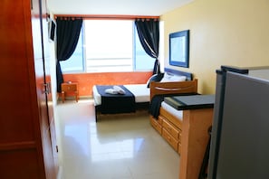 A hotel room with a bed, a desk, a chair, a television, and a window with curtains. - Loft sea View 19C air and Wifi (Cartagena)