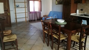 A dining area with a wooden table and chairs, a kitchen with dark wooden cabinets, and a window with sheer curtains. - Apartment Iris 3 Bedrooms,2 Bath, Living Room 10 Pax (Monte Castello di Vibio)