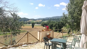 A terrace with a table and chairs, overlooking a scenic landscape with fields and hills. - Apartment Iris 3 Bedrooms,2 Bath, Living Room 10 Pax (Monte Castello di Vibio)