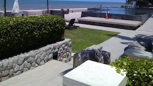 A pool area with a view of the ocean, palm trees, and a stone wall. - Seaview 2 Brs With Chicz Furniture Hua Hin Beach 3 (Cha-am)
