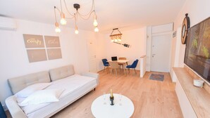 Een moderne woonkamer met een bank, een eettafel met stoelen, een televisie en een kroonluchter.