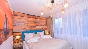 Een slaapkamer met een houten hoofdbord, een bed met witte beddengoed, een nachtkastje met een lamp en dunne gordijnen voor het raam.
