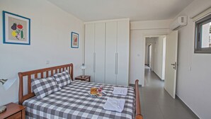 Une chambre à coucher avec une couvre-lit à carreaux, une table de chevet avec une lampe, un tableau encadré représentant des légumes et une armoire avec des portes coulissantes.