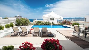 Un espace piscine aménagé sur le toit, avec des chaises longues, une table et un gazebo blanc.