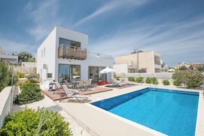 Une maison moderne à deux étages dotée d’une piscine, d’un espace salon extérieur et d’un jardin.