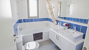 Une salle de bain moderne avec une baignoire, deux lavabos, des toilettes et une fenêtre.