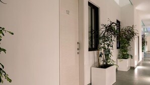 A modern hallway with a white door marked '12', large windows, and potted plants. - Classy 2 Br Apartment Fully Equipped, Up To 5 People, at Aldea Zama (Tulum)