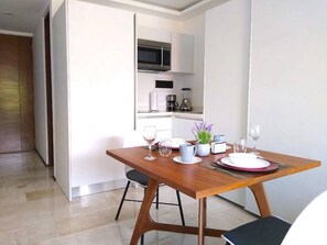 A modern dining area with a wooden table set for two, a kitchen in the background, and a clean, minimalist design.