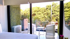 Een slaapkamer met een groot bed, uitzicht op een terras met een stoel en een tafel, en een bloempot op een nachtkastje.