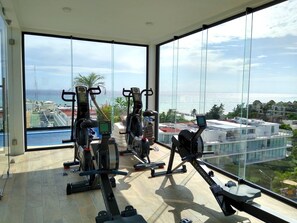 A gym with exercise equipment and a view of the ocean and buildings.
