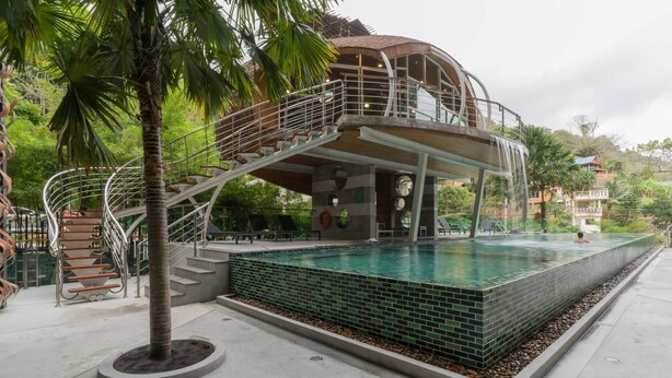 Uma piscina com design moderno, uma escadaria que leva a um andar superior e uma palmeira por perto.