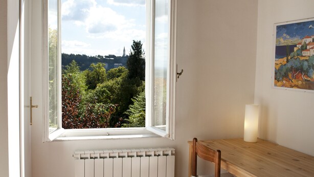 A room with a large window, a wooden table, a chair, a radiator, and a wicker basket. - Perugia Antica Sunny apartment (Perugia)