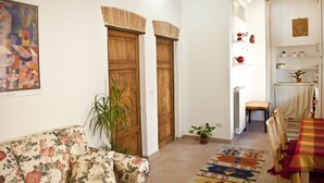 A living room with a floral sofa, wooden doors, a potted plant, and a dining area with a table and chairs. - Perugia Antica Sunny apartment (Perugia)