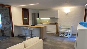 A modern kitchen with a central island, bar stools, and a dining area with a white table and chairs. - Domus Olivarum -costa Smeralda Villetta 7 Persone, 4 PK, Wifi, Grande Giardino (Arzachena)
