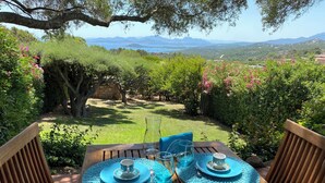 A wooden table with blue placemats and a view of a lush garden and distant mountains. - Domus Olivarum -costa Smeralda Villetta 7 Persone, 4 PK, Wifi, Grande Giardino (Arzachena)