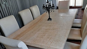 Een rechthoekige eettafel met een licht houten afwerking, omringd door zes witte, beklede stoelen.