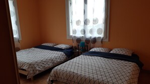 Une chambre avec deux lits, chacun recouvert d’une couvre-lit à motifs géométriques, une petite table avec une lampe et une fenêtre avec un rideau.