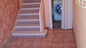 Un escalier menant à une buanderie équipée d’un lave-linge et d’un radiateur.