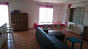 Un salon avec un canapé, une table à manger avec des chaises, un coin cuisine avec des placards et une fenêtre avec des rideaux.