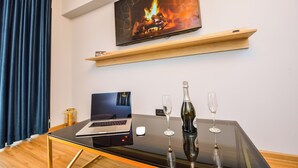 Een moderne kamer met een televisie waarop een haard te zien is, een laptop op een glazen tafel en twee glaasjes.
