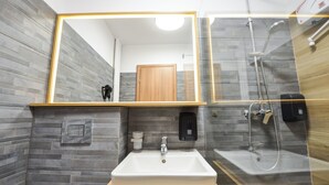Een badkamer met een grote spiegel, een wastafel, een douche en een houten wastafelmeubel.