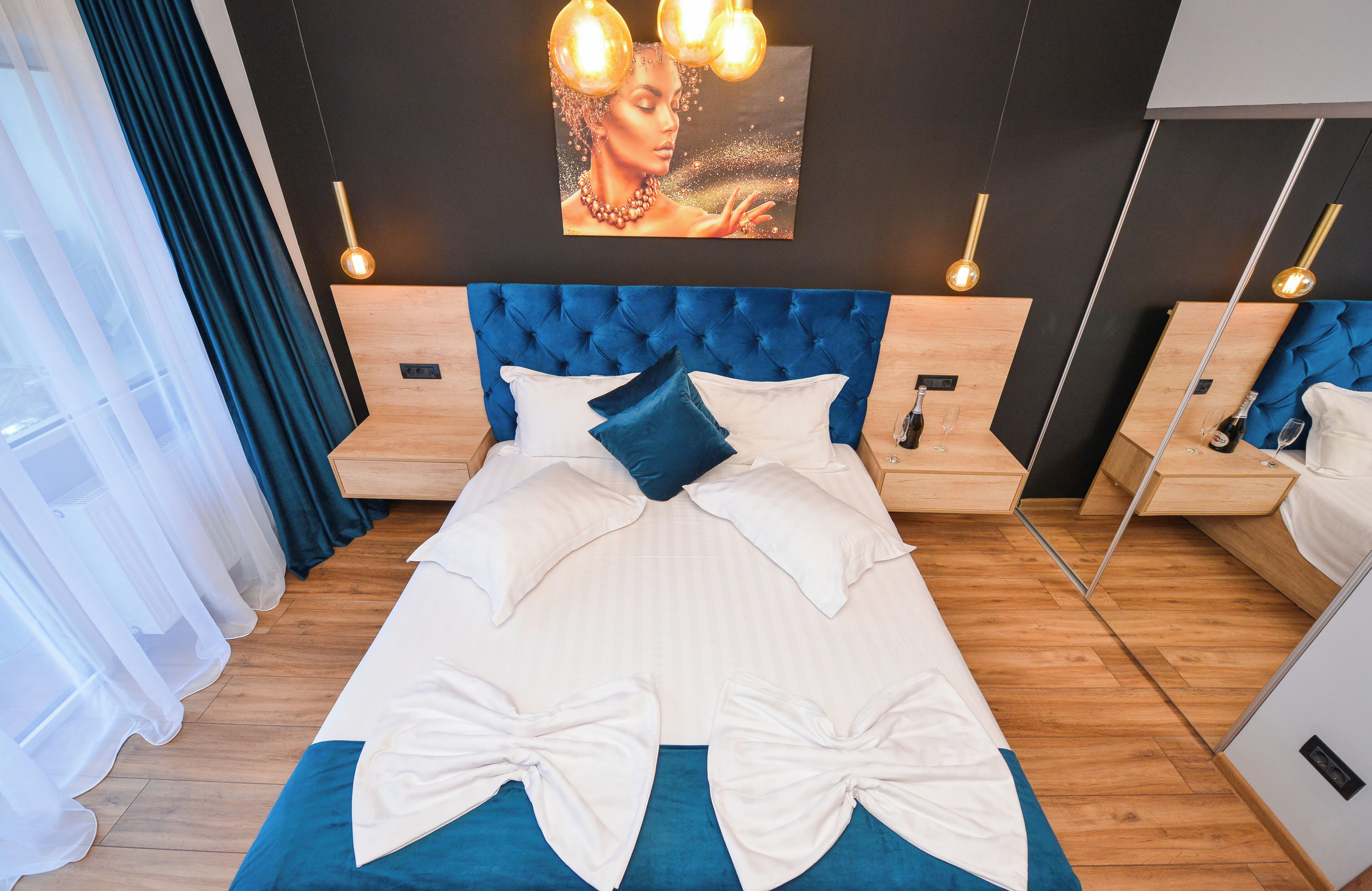 A modern bedroom with a tufted headboard, a large bed with white and blue bedding, two bedside tables, and a wall-mounted light fixture.