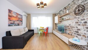 Una sala de estar moderna con un sofá negro, sillas coloridas, una mesa redonda, un televisor y una pared con diseño de ladrillo.