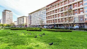 Un edificio grande con varios pisos, rodeado de un césped bien cuidado y varias aves.