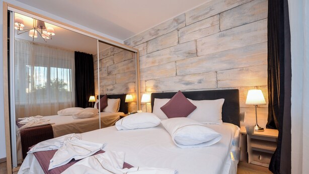 Una habitación de hotel con una cama grande, un espejo, dos mesitas de noche con lámparas y una pared de madera.