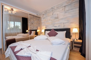A hotel room with a large bed, a mirror, two bedside tables with lamps, and a wooden wall. - Bucharest Apartment - Two Bedrooms - 6 Guests - Cismigiu Gardens (Bucharest)