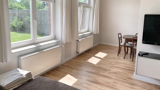 Een kamer met grote ramen, een eettafel met stoelen, een televisie en een radiator.