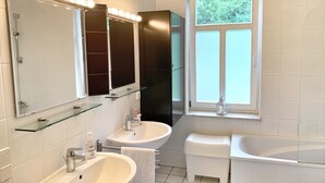 Een moderne badkamer met twee wasbakken, een wastafelmeubel, een spiegel met verlichting, een raam en een bad.