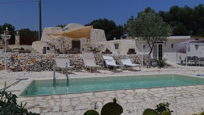 A pool area with stone walls, lounge chairs, and a shaded area. - Trullo Dell Orto Ostuni (Ostuni)