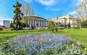 Ein großes Gebäude mit einer geschwungenen Fassade, umgeben von einer gepflegten Rasenfläche mit verschiedenen Blumen und Bäumen.