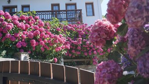 A white building with a balcony, surrounded by pink and purple flowers.