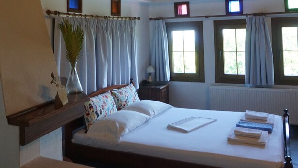 A bedroom with a wooden ceiling, a bed with white linens, a nightstand, a lamp, and a window with curtains.