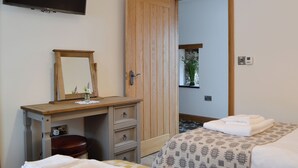 Une chambre d’hôtel avec un bureau en bois, une télévision, une armoire, un lit avec des serviettes et une petite fenêtre agrémentée d’une plante.