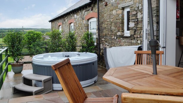 Une construction en pierre dotée d’un jacuzzi, d’une terrasse en bois et d’un espace salon extérieur.