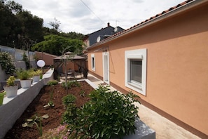 Enjoy a serene garden oasis with a patio and outdoor furniture, surrounded by lush greenery and a low wall.