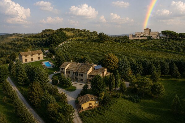 A villa surrounded by lush greenery and vineyards, with a castle in the background and a rainbow.
