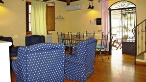 Una habitación con techo de madera, una mesa de comedor con sillas, una cama con cubrecama azul con lunares y una escalera que conduce a un área exterior.