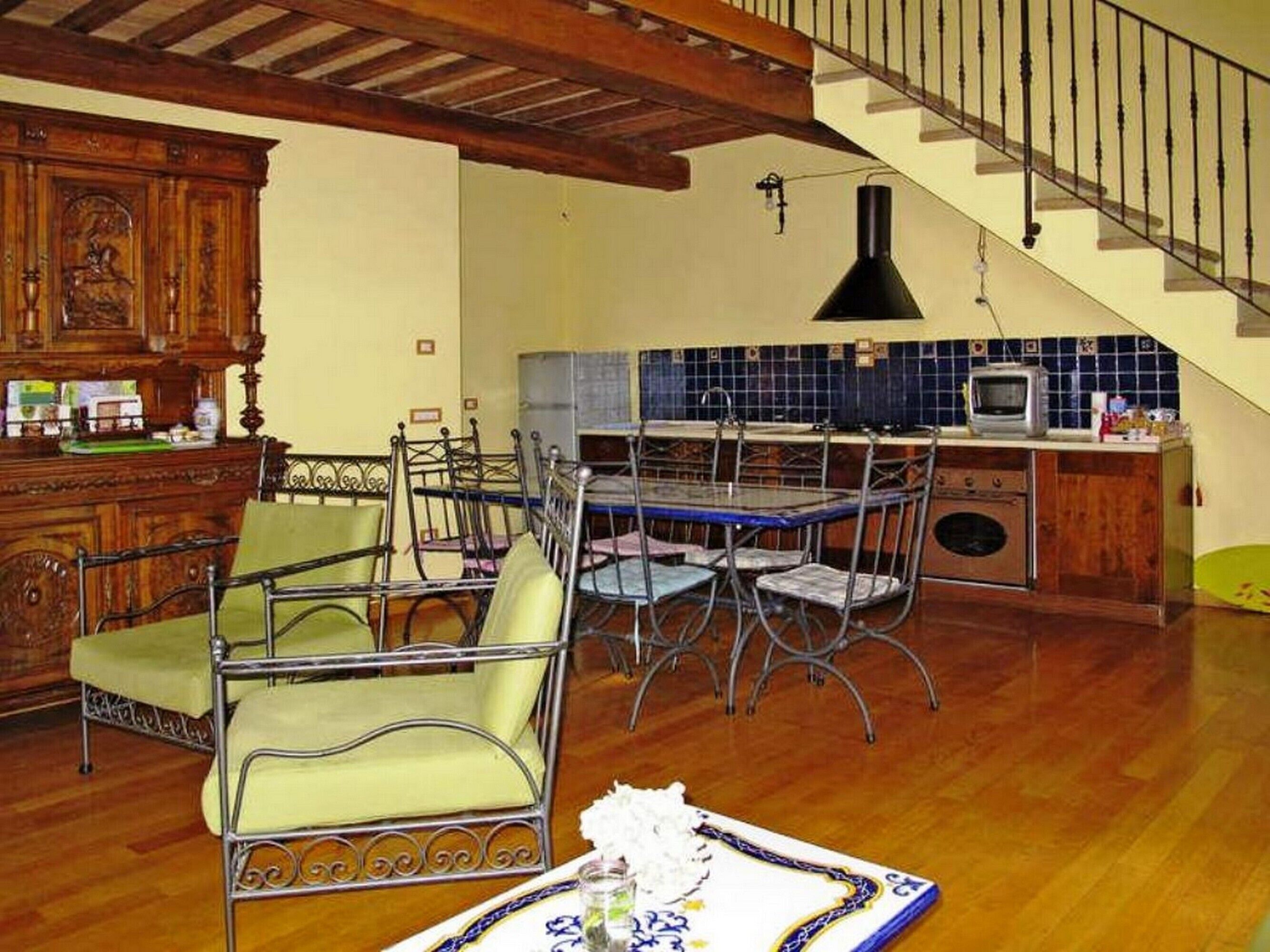 Un coin repas avec une table et des chaises, une cuisine avec un mur recouvert de carreaux, et un escalier.