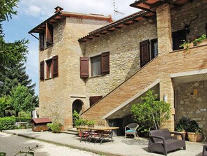 A stone building with a sloped roof, a staircase leading to the upper floor, outdoor seating, and a small covered area. - Podere Caldaruccio La Pineta - 26 People Cottage e Villa (Perugia)