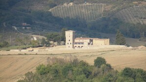 Un edificio rural con una torre, rodeado de campos y árboles.