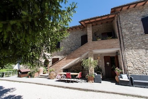 A stone building with a wooden staircase leading to a balcony. There is outdoor seating with red chairs and a table. - Podere Caldaruccio La Pineta - 26 People Cottage e Villa (Perugia)