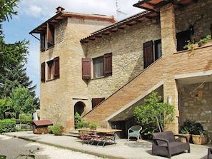 Un edificio de piedra con techo inclinado, una estructura pequeña adosada y mesas al aire libre.