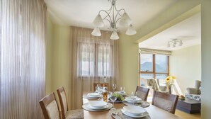 A dining area with a wooden table set for four, a chandelier, and a view of mountains through a window. - TIVAT apartment (NO-9) (Donja Lastva)