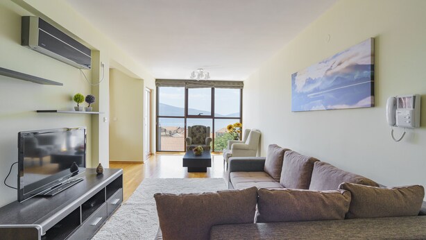 A modern living room with a flat-screen TV, a sofa, and a coffee table. There is a large window with a view of the outdoors. - TIVAT apartment (NO-9) (Donja Lastva)
