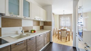 A modern kitchen with a central island, a dining area with a chandelier, and a view into the living room. - TIVAT apartment (NO-9) (Donja Lastva)