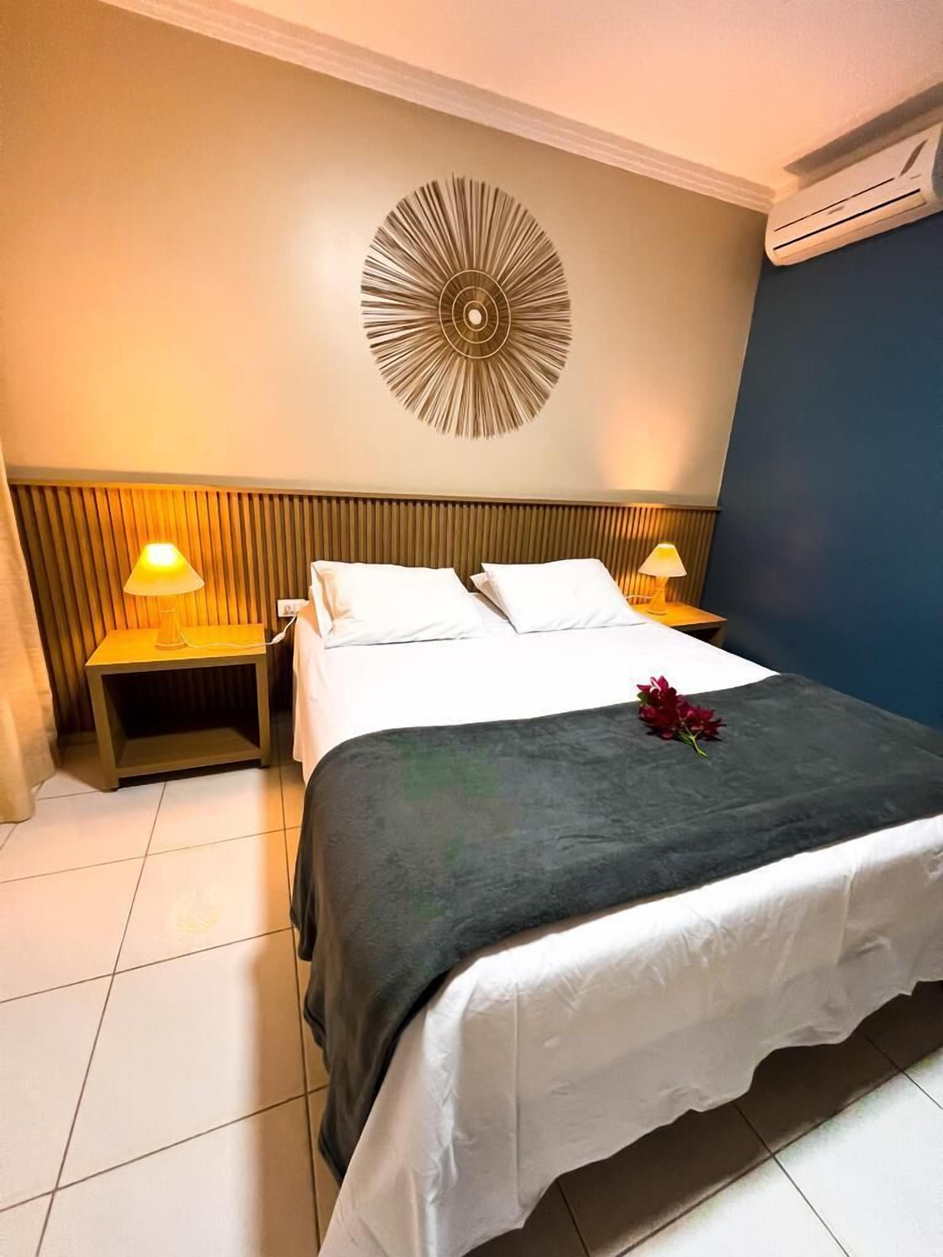 A hotel room with a bed, two bedside lamps, a wall-mounted decorative piece, and an air conditioning unit.